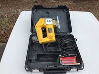 Top view of yellow DEWALT orbital jig saw in its black carrying case, showing power cord and additional saw blades packaging inside the case.