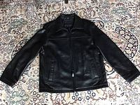 Front view of the black Dockers leather jacket laid flat on patterned carpet, showing zipper front, collar, and side pockets.