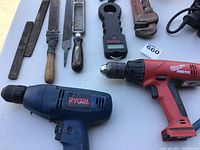 Two electric drills: Ryobi and Milwaukee Power Plus, with some hand tools including files and scale.