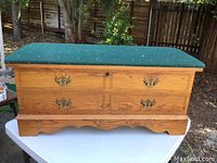 Front view of cedar chest showing two drawers with ornate brass handles and green upholstered cushioned top