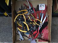 Overview of assorted used pliers in cardboard box, showing variety and handle colors