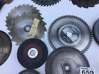 Close-up of several circular saw blades and one black abrasive cutting disc arranged on a white surface.