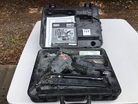 Senco pneumatic nailer and accessories placed inside a molded black plastic carrying case on white background.