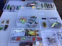 Overview photo showing several small plastic boxes on a table containing multiple fishing lures and tackle items
