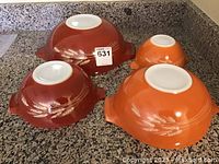 Four vintage Pyrex Cinderella mixing bowls with Harvest wheat design, showing bottoms and wheat design on brown and orange bowls