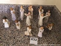 Photo showing all 12 Willow Tree figurines arranged on a granite surface, depicting various angel and contemplative poses with wire wings and hand-carved details.