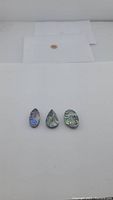 Front view of three pear-shaped abalone doublet gemstones laid flat on white background, showing distinct iridescent colors and patterns.
