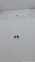 Pair of round natural emerald stud earrings on white background, showing green cabochon stones in bezel sterling silver setting.