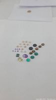 Photo shows a spread of mixed natural gemstones organized on a white background including amethyst, black onyx, green onyx, pink opal, tiger's eye, malachite, and citrine stones in various shapes and sizes.