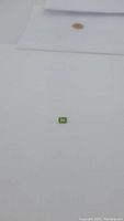 Small emerald cut apple green peridot gemstone placed on white background, showing shape and color