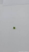 Natural apple green peridot gemstone in cushion checker cut, placed on a plain white background for clear view.