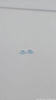 Two small light sky blue oval cut topaz gemstones side by side on grey background showing size and shape