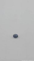 Natural blue oval cut sapphire gemstone on white background, showing polished surface, measured size, and some inclusions visible.