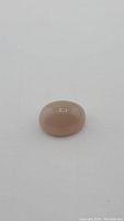 Top-down image of a smooth, oval cabochon cut peach moonstone with a domed surface showing translucency and color.