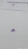 Single pear cut natural amethyst gemstone lying on white surface, showing top and side views.