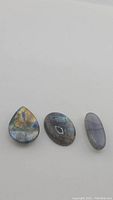 Wide view of three polished labradorite stones showing varying shapes and labradorescence