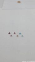 Seven round cabochon cut tourmaline gemstones in various colors including blue, pink, peach, and purple, displayed on white background