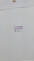 Top-down clear image of 16 small round amethyst cabochons arranged in four rows against a white background, showing light purple hues and dome surface.