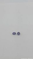 Two natural untreated purple iolite gemstones on white background, one oval cut and one diamond cut