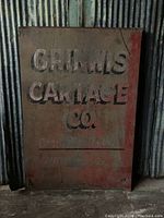 Full view of the rectangular metal sign showing faded red background and embossed white and black lettering 'CRIMW'S CARTAGE CO.', with aging and rust marks visible.