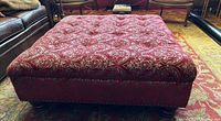 Front view of large square ottoman with red damask upholstery and tufted top, wooden feet detached and placed underneath.