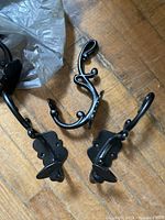 Group of 3 black metal wall hooks on wooden floor showing different styles and mounting plates