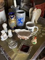 The full lot shown on a gold table, includes vase, beer stein, ceramic angel, mug, dish, bell, ashtray, and several figurines.