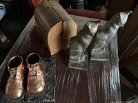 Photo showing three pairs of vintage bookends including bronze baby shoes on marble, black metal cats, and wooden shapes.