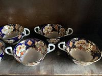 Five oval-shaped two-handled Royal Albert Crown China cups with floral and gold pattern on cobalt blue background