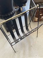 Front and side view showing open structure with five curved metal bands supporting magazines and a differing finish metallic top bar, overall slender tall legs.