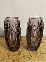 Two vintage purple glass vases side by side on a table showing front and side designs