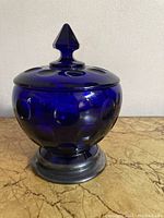 Frontal image of the cobalt blue glass dish with lid, showcasing the circular dot pattern and silver base with dent.
