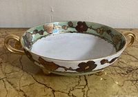 Side view of vintage round dish showing gold scroll handles and floral iridescent green border