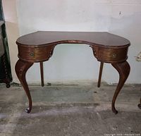 Front view of vintage kidney-shaped vanity desk showing wooden top, two curved drawers and cabriole legs.