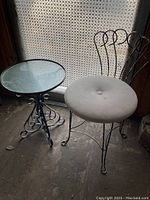Full view of vintage metal chair with cushioned seat and metal side table with glass top, showing the intricate metalwork and overall condition.