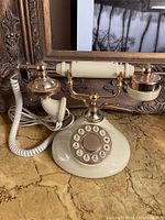 Front angle view of vintage cream and gold-tone pushbutton rotary dial telephone, showing handset and cord.