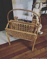 Front angle view of vintage rattan magazine rack showing woven rattan design and magazines inside.