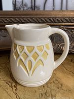 Side view showing the diamond and teardrop pattern with mustard glaze on cream pottery pitcher.