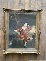 Full view of the vintage shadowbox framed portrait print showing the ornate gold-tone frame and the seated young boy in a red velvet suit.