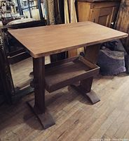 Full view of vintage solid wood side table with trestle base and shelf on wooden floor, shows shapes and structural details.