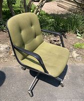 Front-side view of the vintage Steelcase chair showing green fabric upholstery, black armrests, metal frame, and caster wheels.