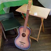 Photo showing Edmond acoustic guitar leaning against folding rocking stool and TV tray table in background on wooden floor
