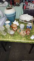 Table with various pottery and decorative items including tall vase, shell-shaped bowl, small pots, and figurines