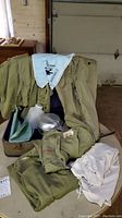 Overall view of vintage Boy Scout uniform pieces including shirts, pants, apron, neckerchief, mess kit, and suitcase.