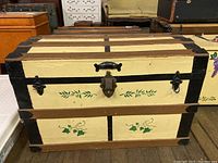 Front view of the wooden chest showing painted floral design, metal lock and latches, and missing side handles.