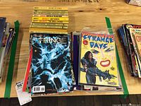 Top view of a stack of comic books including Fringe and Strange Days on a wooden surface.