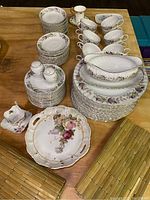 Photo of 66-piece Creative Regency Rosa china set with plates, cups, saucers, serving bowls, gravy boat, and salt and pepper shakers along with 5 bamboo placemats on wooden table.