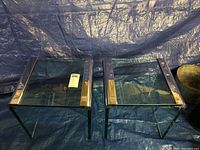 Photo showing two glass and chrome side tables side by side on a blue tarp