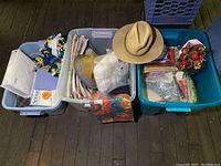 Three totes on the floor filled with various items including a straw hat on top, sewing supplies, folded fabrics, and Christmas decorations.