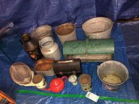 Full lot displayed on blue tarp including metal buckets, jugs, ceramic teapot, fencing helmet, smoker, lunch box, coffee cans.